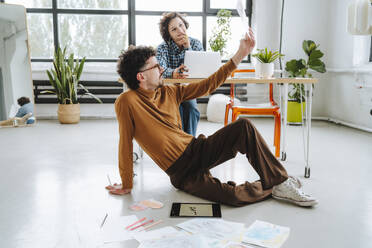 Designer examining designs with coworker sitting at office - MDOF01645