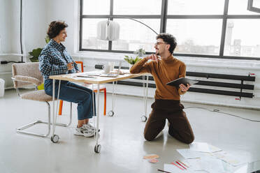 Junger Designer im Gespräch mit einem Kollegen, der am Schreibtisch im Büro sitzt - MDOF01646