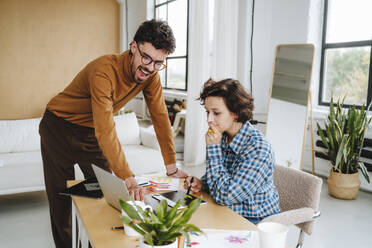 Illustrator explaining colleague over laptop sitting at desk in office - MDOF01649