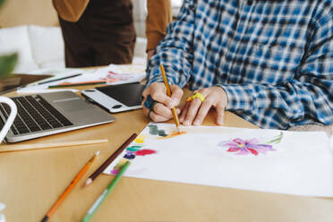 Young graphic designer coloring on paper at desk in office - MDOF01652