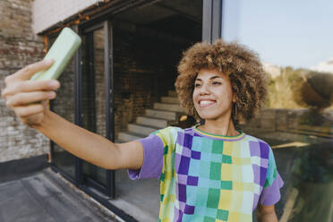 Smiling woman taking selfie through smart phone in balcony - YTF01414