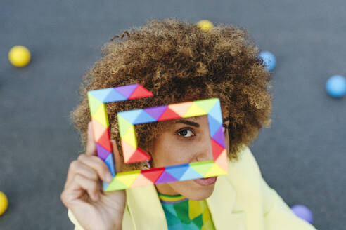 Woman with curly hair looking through colorful toy - YTF01428