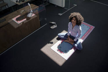 Geschäftsfrau meditiert auf Yogamatte im Büro - KNSF09956