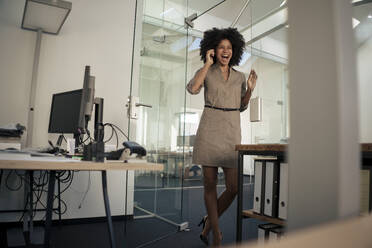 Happy businesswoman talking on smart phone standing near door at office - KNSF09969