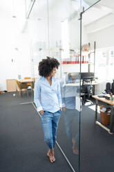 Businesswoman looking through glass wall at office - KNSF09979