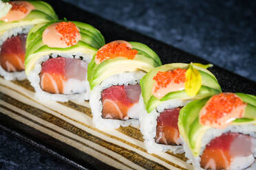 Closeup of appetizing tobiko roe with fresh green avocado slices on top of uramaki sushi rolls served on tray on marble counter - ADSF48821