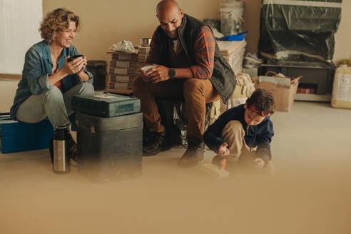 Eine Familie, die an einer Heimwerker-Renovierung arbeitet, macht eine Kaffeepause. Die Eltern sitzen mit ihrem kleinen Sohn im Haus und ruhen sich aus. Ihre Teamarbeit bei der Renovierung ihres Hauses zeigt, dass sie sich der Schaffung eines komfortablen Heims verschrieben haben. - JLPSF30922