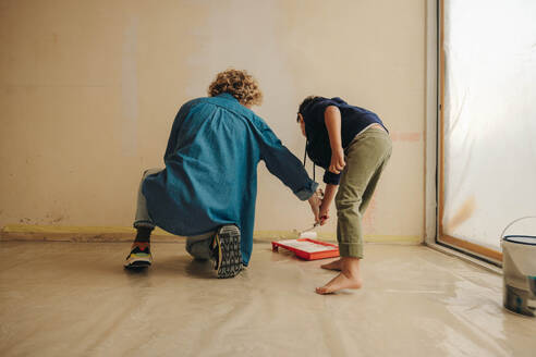 Creative, caucasian mother and her young son painting an interior wall together, renovating their home. This DIY project showcases their dedication to home improvement and their teamwork as a family. - JLPSF30923