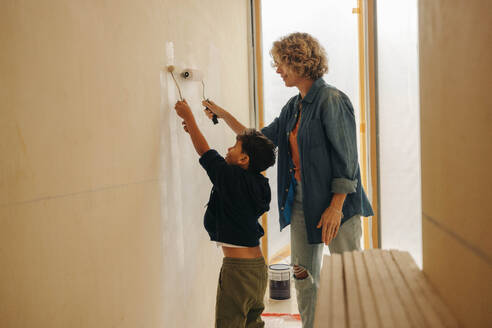 DIY activity at home with a Caucasian mother and her young son painting an interior wall together. Mom and child engaging in a home renovation and demonstrating their creativity. - JLPSF30924