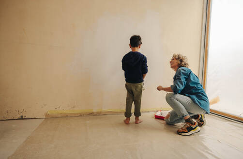 Supportive mother talking to her son, cheering him up during home renovation. Mom and son painting the interior walls to bring life and colour to their house and create an inviting atmosphere. - JLPSF30927