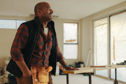 Ein älterer Mann steht in einer Küche, die gerade renoviert wird. Er trägt einen Werkzeuggürtel und lächelt, während er an der Modernisierung arbeitet. Seine Heimwerkerkenntnisse sorgen für ein erfolgreiches Heimwerkerprojekt. - JLPSF30933
