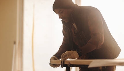 Der Zimmermann misst ein Holzbrett für die Hausrenovierung aus. Der Facharbeiter arbeitet im Haus mit Präzision. Mit einem Maßband sorgt er für genaue Messungen für das Bauprojekt. Das Fachwissen des Bauunternehmers in der Schreinerei und der Hausrenovierung ist offensichtlich, als er die Fußleisten verbessert. - JLPSF30951