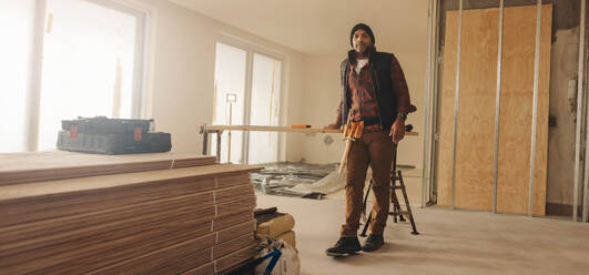 Mature building contractor with a tool belt stands in a kitchen, ready to renovate. This skilled worker specializes in home improvement and remodelling, offering expertise in carpentry and flooring. - JLPSF30959