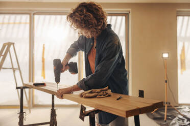 Ältere Bauarbeiterin bei der Renovierung eines Hauses: Mit einer Bohrmaschine bringt sie Fußleisten in der Küche an. Ein erfahrener Bauunternehmer renoviert und verschönert den Innenraum mit Holzarbeiten. - JLPSF30966