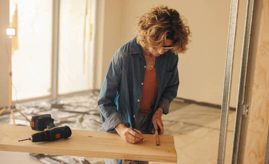 DIY homeowner, a mature woman, measures baseboard in her kitchen for a remodeling project. Using a tape measure, she marks and prepares for the renovation, displaying carpentry skills and dedication to home improvement. - JLPSF30967