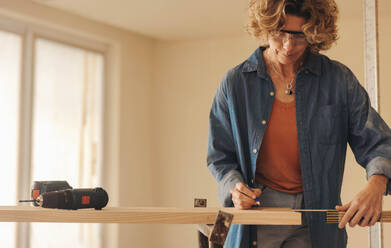Ältere Frau, die an einer Küchenrenovierung arbeitet. Sie misst und markiert die Sockelleisten mit Maßband und Bleistift. Sie ist eine erfahrene Schreinerin und Heimwerkerin und konzentriert sich darauf, ein makelloses Ergebnis zu erzielen. - JLPSF30968