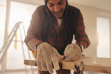 Ein Bauunternehmer misst und markiert eine Diele für eine Küchenrenovierung. Mit Fachkenntnis arbeitet er an den Fußleisten und den Tischlerarbeiten und wertet das Innere des Hauses mit geschickten Holzarbeiten und handwerklichem Geschick auf. - JLPSF30974