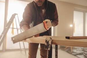 Ein Zimmermann schneidet bei der Renovierung eines Hauses ein Holzbrett zu. Der Facharbeiter arbeitet in einem Innenraum und renoviert den Küchenbereich mit einer Kappsäge. - JLPSF30975