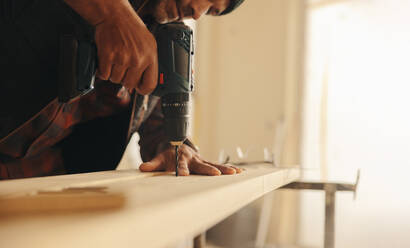 Carpenter uses a drill gun to attach wood baseboards in a house kitchen. This professional contractor leads the upgrade and refurbishment of the interior, showcasing expertise in construction and remodeling. - JLPSF30987