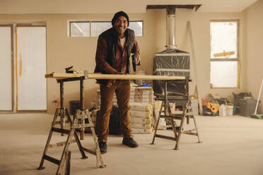 Hausbesitzer, der sein Haus renoviert, lächelt, während er Fußleisten bohrt und das Innere mit geschickten Holzarbeiten aufwertet. Älterer Mann, der seine Küche mit Heimwerkerausrüstung und Werkzeugen renoviert. - JLPSF30991