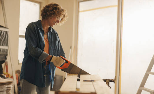 Eine erfahrene reife Frau schneidet mit einer Kappsäge ein Holzbrett für Fußleisten zu. Sie renoviert das Innere eines Hauses und demonstriert damit ihr Fachwissen in der Tischlerei und im Heimwerken. - JLPSF30994