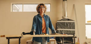Ältere, geschickte Frau mit Schutzbrille renoviert eine Küche mit Holzpaneelen. Ihr glücklicher Gesichtsausdruck spiegelt ihr Fachwissen wider, während sie die Inneneinrichtung in diesem Heimwerkerprojekt aufwertet. - JLPSF31000