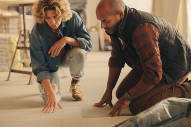 Homeowners collaborating on a home renovation. They discuss and plan the redesign of their kitchen's flooring tiles. Married couple working together, focusing on the DIY project. Their teamwork showcases their dedication to upgrading their home. - JLPSF31006