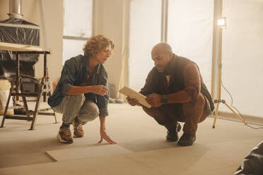 Husband and wife working on home improvement, collaborating in their kitchen. They discuss ideas, plan renovations. Teamwork can be seen as they choose flooring tiles, upgrading their house together. - JLPSF31008