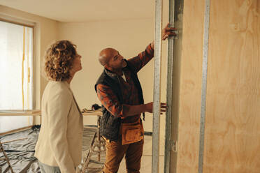 Ein Bauunternehmer und ein Hausbesitzer besprechen eine Innenrenovierung, bei der sie sich auf den Türrahmen konzentrieren wollen. Die Zusammenarbeit zwischen dem professionellen Handwerker und dem Hausbesitzer zielt auf eine erfolgreiche Verbesserung des Hauses ab. - JLPSF31026