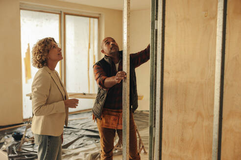 Construction worker and house architect discussing interior remodeling plans. They collaborate on a renovation project for a house, focusing on redesigning and refurbishing the interiors. - JLPSF31028