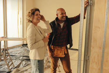Male builder and female architect collaborate on a home renovation project. They discuss the remodel inside a house, near a doorframe. The contractor's expertise and the homeowner's input ensure a successful property upgrade. - JLPSF31029