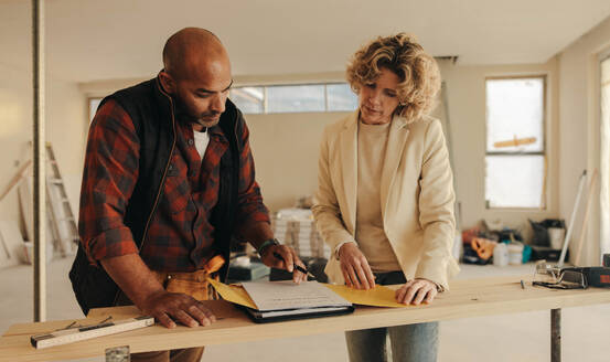 Ein älterer Bauunternehmer und eine Hausbesitzerin unterzeichnen in einem Haus einen Vertrag für ein Renovierungsprojekt. Sie demonstrieren Professionalität und Hingabe an ihre Arbeit, um eine erfolgreiche Renovierung zu gewährleisten. - JLPSF31038