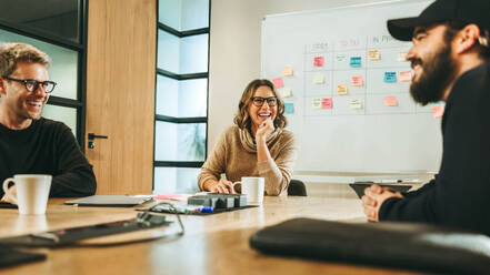Business professionals, both men and women, collaborate in a modern boardroom. Engaged in a lively discussion, they brainstorm ideas with a diverse team. Smiling and happy faces depict a successful startup's dynamic and creative atmosphere. - JLPSF31067