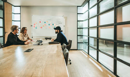 Professionals engage in a dynamic discussion in a modern boardroom. Diverse colleagues collaborate on a project, following the scrum process. A creative and professional atmosphere fosters teamwork and idea exchange among the group. This tech company promotes productivity and effective communication. - JLPSF31068