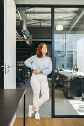 Confident redhead businesswoman ponders at her office, portraying a dedicated employee in the tech industry. Her appearance exudes confidence and professionalism, reflecting the lifestyle of a successful business person. - JLPSF31082