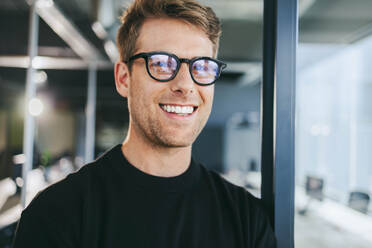 Confident male professional in office setting. Business man with glasses smiling at camera. Tech professional actively working in workplace. Successful entrepreneur exuding happiness and confidence. - JLPSF31083