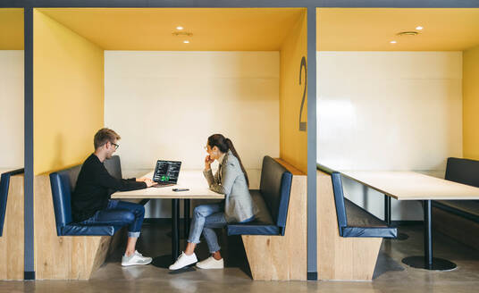 Colleagues in a coworking office discuss a software design and programming project. Coding experts working remotely, using a laptop. Teamwork drives efficient software development in this productive workplace. - JLPSF31084