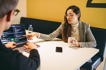 Coding professionals, a man, and a woman, code and collaborate in a modern office. They discuss software design, showcasing teamwork and expertise. This image represents business, technology, and a professional lifestyle. - JLPSF31087
