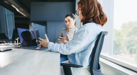 Female colleagues actively collaborate in a modern office, engaging in discussions, coding and programming. Skilled women creating innovative software solutions in a workplace that showcases teamwork and cutting-edge technology. - JLPSF31091