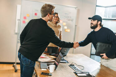Two software developers shaking hands to solidify a deal on a software development project. Business professionals engaging in a productive meeting focused on teamwork and partnership. - JLPSF31107