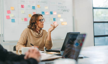 Eine Frau bei einem gemeinsamen Brainstorming mit ihren Kollegen in einem Sitzungssaal. Geschäftsleute diskutieren Ideen und verwalten Projekte. Sie arbeiten gemeinsam an der Softwareentwicklung und dem Projektmanagement in einem Technologieunternehmen. - JLPSF31110