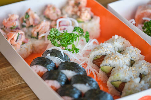 Set of appetizing sushi rolls with fresh fish and daikon with parsley served in carton box on table in restaurant with Asian food - ADSF48864