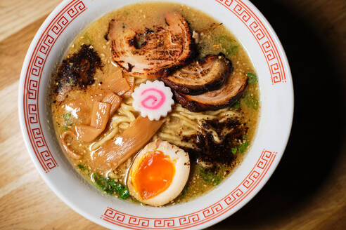 Top view of traditional Asian ramen soup with noodles and egg served in white ceramic bowl on wooden table - ADSF48866