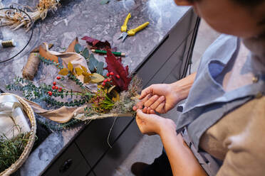 From above side view of unrecognizable female florist tying bunch of flowers on table while making bouquet at work - ADSF48883