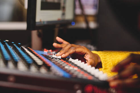 Unrecognizable crop African American woman in yellow sweater using mixing panel with control buttons while working in broadcast studio - ADSF48891