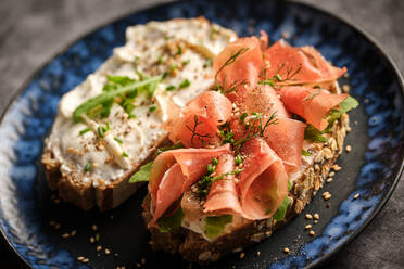 From above of delicious bruschetta with jamon slices and cream cheese served on plate on wooden table - ADSF48910