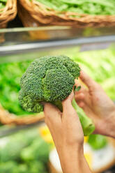 From above crop unrecognizable person holding fresh broccoli against blurred background of food market - ADSF48939