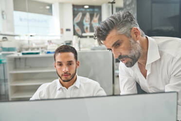 Focused bearded professional male engineers in formal wear browsing computer while discussing project during work in modern light spacious office - ADSF48965