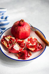 A ripe pomegranate open on a blue-trimmed plate, revealing its red seeds, accompanied by a wooden handled knife.. - ADSF48995