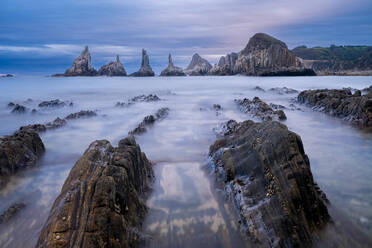 Long exposure of waves washing over rocks and cliffs against cloudy sky in Asturias, Spain - ADSF49045